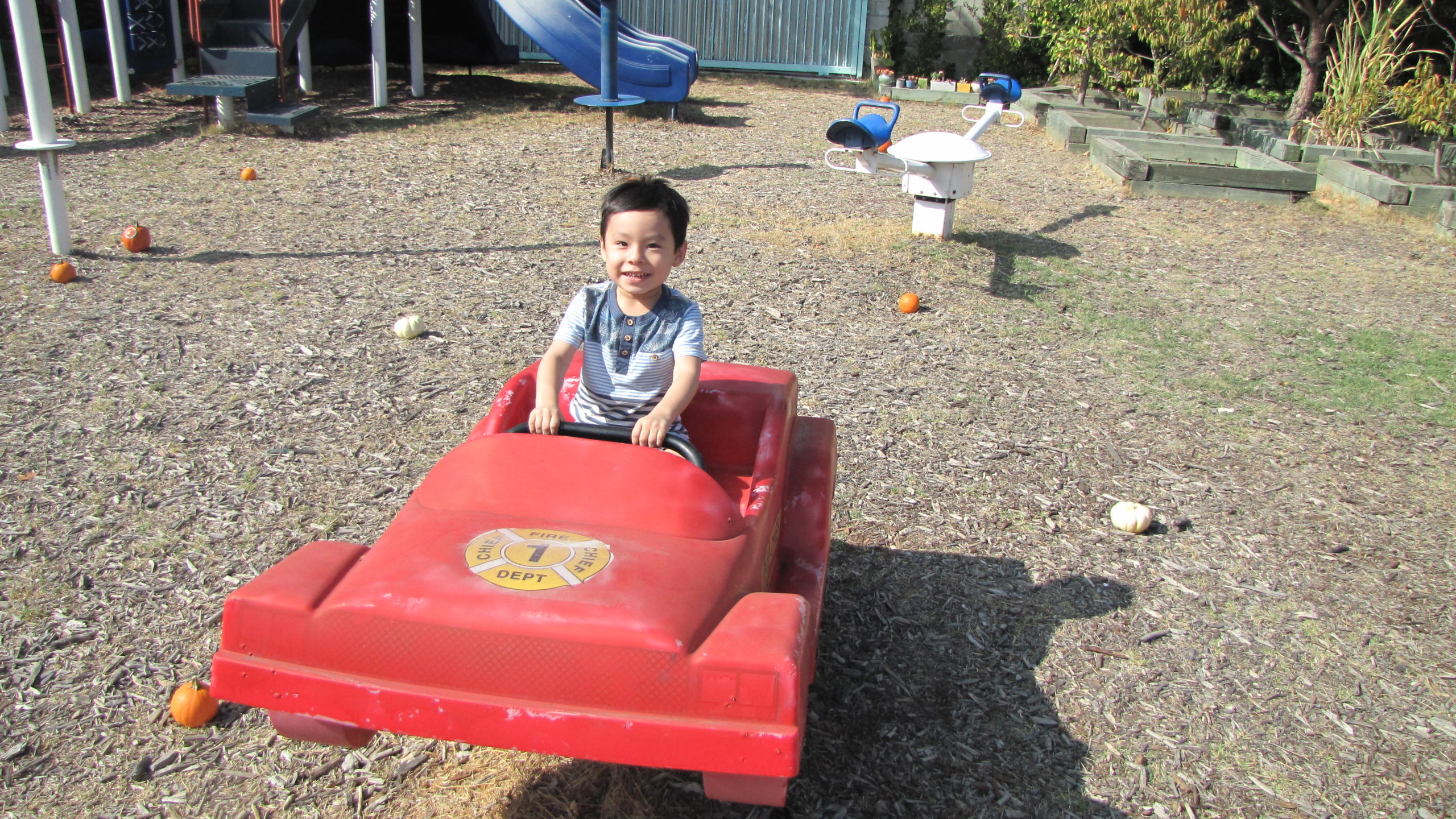 A young boy in a red car at a playground.